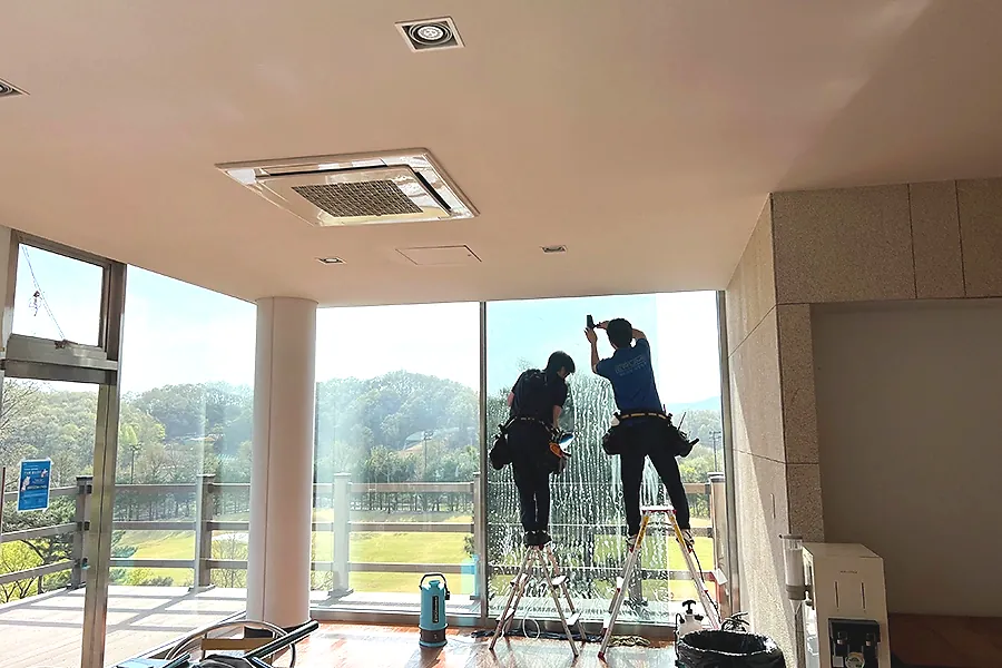 골프장 라운지 통유리 열차단필름 시공 중 사다리 작업 모습