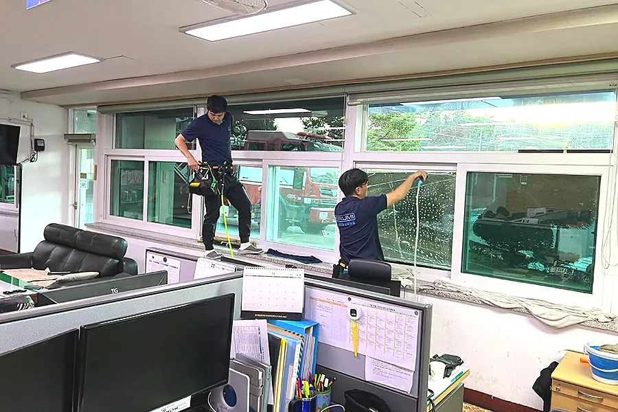 공공기관 사무실 대형 창호 열차단필름 시공 중 작업자가 필름을 부착하는 모습