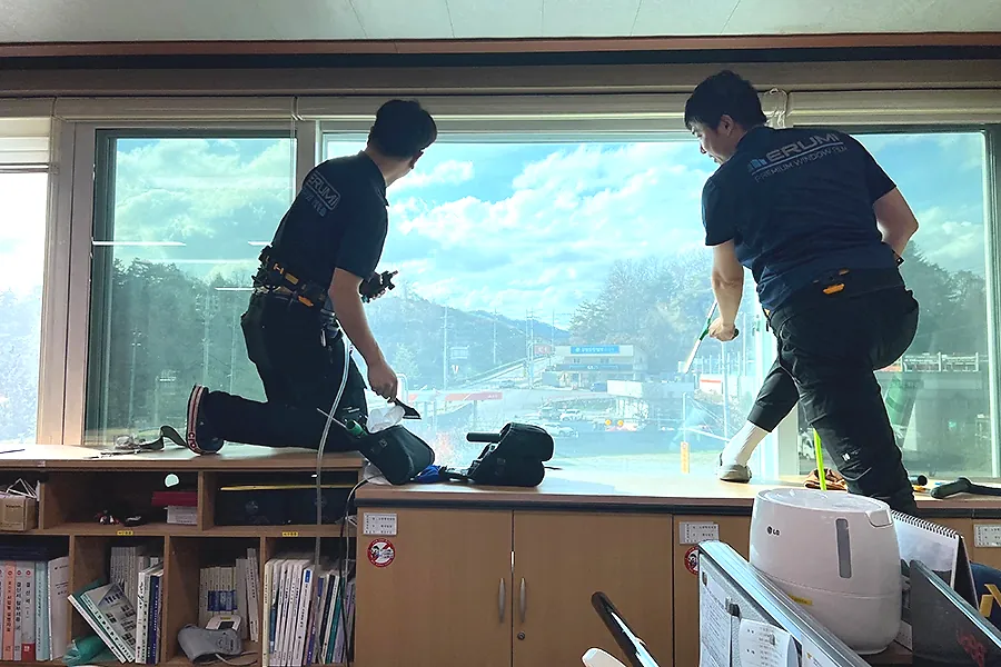 공공기관 대형 유리창 열차단필름 시공 과정, 두 명이 함께 작업하는 모습